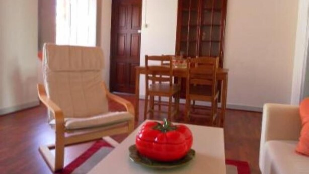 Una sala de estar con una mesa de comedor de madera, un sillón beige y un adorno rojo sobre una mesa blanca.