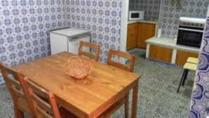 Cocina compacta con microondas, horno y un refrigerador pequeño. Hay una mesa de madera con sillas y una cesta encima.