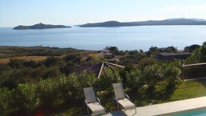 Vista a la piscina con sillas de descanso, una visión despejada del mar e islas a lo lejos.