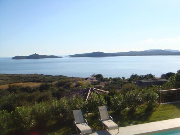 A poolside view with lounge chairs, a clear view of the sea, and distant islands.
