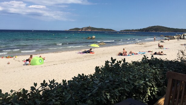 Una playa con gente tomando el sol y nadando, una sombrilla verde, y afloramientos rocosos al fondo.