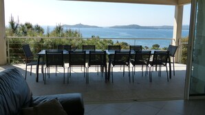 Un balcón con mesa y sillas que ofrece vistas panorámicas del mar y las colinas.