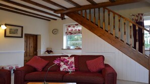 A cozy living room with a wooden staircase, a red sofa, a clock, and a window with floral curtains. - Detached Rural Cottage in Idyllic Location with 3 acre safe secure 6ft dog field (Bradnop)