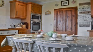 A kitchen with wooden cabinets, a microwave, an oven, and a dining table set with white dishes and a green teapot. - Detached Rural Cottage in Idyllic Location with 3 acre safe secure 6ft dog field (Bradnop)