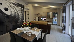 Un espace repas moderne avec un motif géométrique sur le mur, une table en bois recouverte d’une nappe en dentelle et un canapé en arrière-plan.