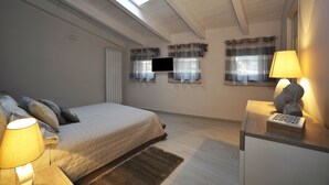 Une chambre à coucher avec un lit, des lampes de chevet, une télévision et une fenêtre avec des rideaux.