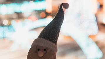 Un peluche de Papá Noel frente a una ventana, con un árbol de Navidad y luces desenfocadas al fondo.