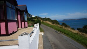 A coastal road with houses, a white fence, and a clear view of the sea. - Brynsior, Chalet on the hill in Goodwick with stunning sea views (Fishguard)