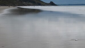 A wide sandy beach with gentle waves, a grassy hill in the background, and a cloudy sky. - Brynsior, Chalet on the hill in Goodwick with stunning sea views (Fishguard)