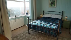 A bedroom with a bed, a window, a radiator, and a nightstand with a lamp. - Brynsior, Chalet on the hill in Goodwick with stunning sea views (Fishguard)