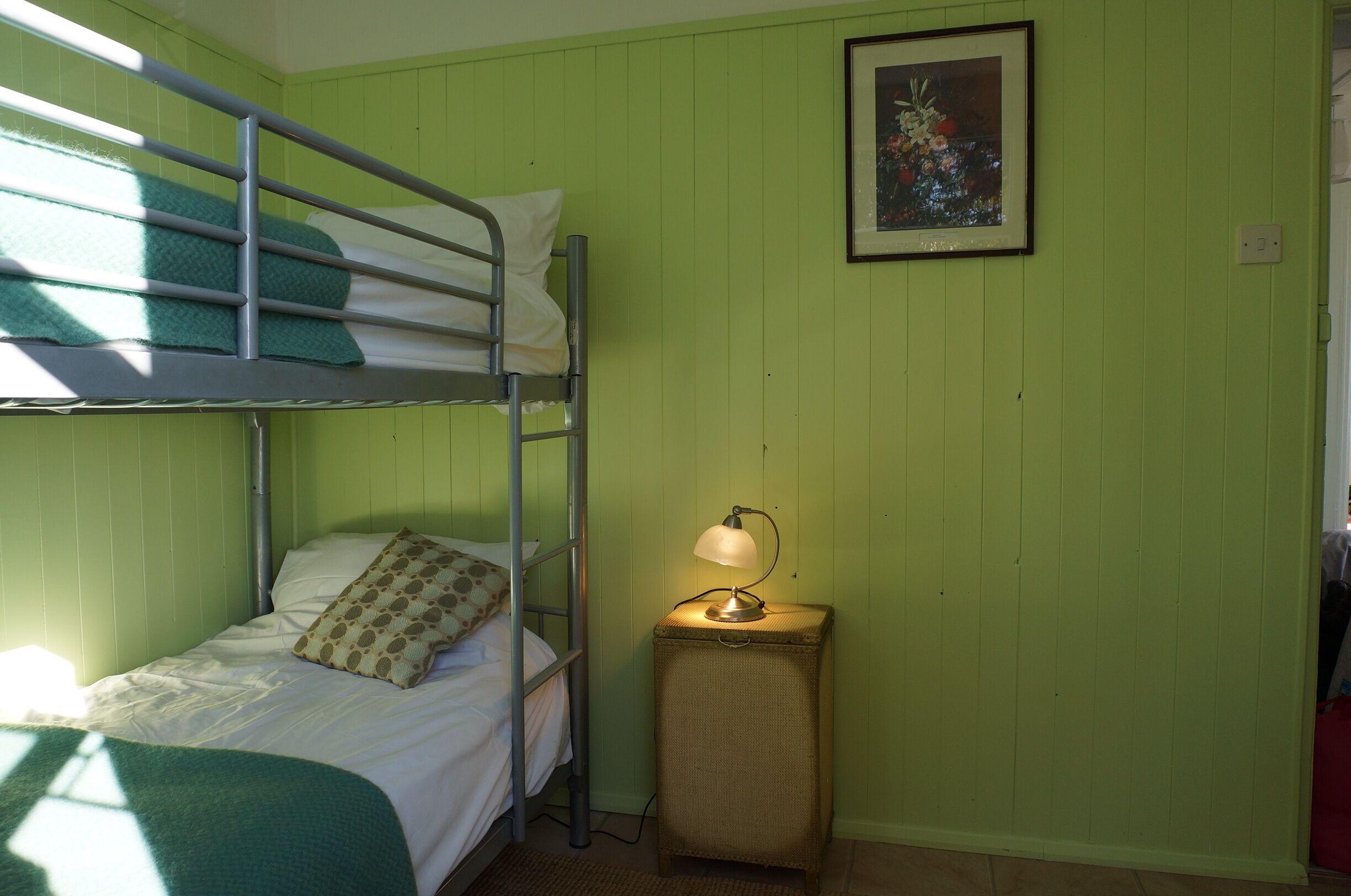 Habitación con literas, una mesita de noche pequeña y una lámpara, paredes verdes y un cuadro enmarcado en la pared.