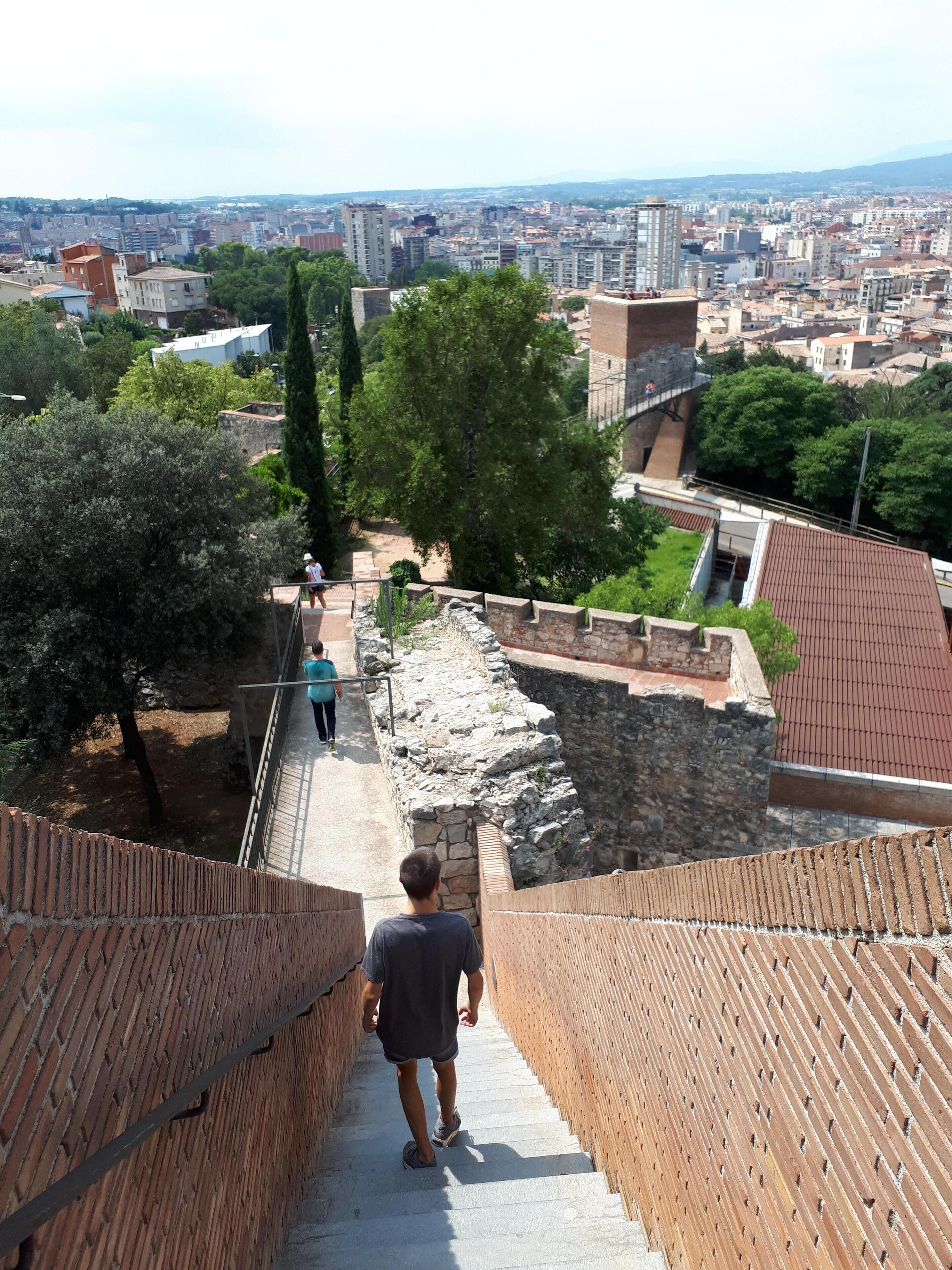 Un camino que lleva a un sitio histórico con muros de piedra y vistas de un paisaje urbano al fondo.