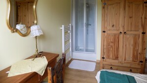 Un dormitorio con un aparador de madera, un espejo, una mesita de noche con una lámpara, una ducha y un armario.