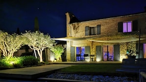 A modern house with a patio, outdoor seating, and a well-lit garden area at night. - Charming house with swimming pool and air conditioning 15 minutes from Bordeaux (Saint-Caprais-De-Bordeaux)