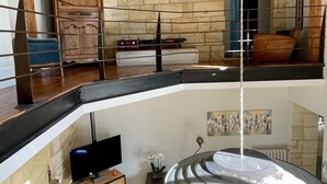 A multi-level living space with exposed wooden beams, a stone wall, a fireplace, a television, and a hanging light fixture. - Charming house with swimming pool and air conditioning 15 minutes from Bordeaux (Saint-Caprais-De-Bordeaux)