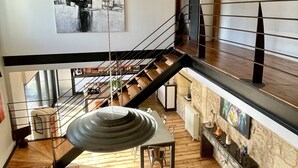 A spacious loft with a high ceiling, exposed wooden beams, a mezzanine level, a staircase, a dining area, and a living room with a gray sofa. - Charming house with swimming pool and air conditioning 15 minutes from Bordeaux (Saint-Caprais-De-Bordeaux)