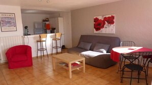 Een woonkamer met een bank, een rode stoel, een houten salontafel en een eettafel met stoelen. Achtergrond is een keukenhoek.