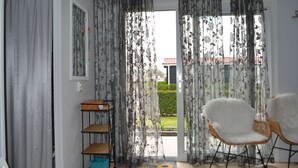 A room with a sliding glass door, a wicker chair, a small wooden shelf, and a mat on the floor. - Chalet Zonnebloem for 6 people, lots of privacy in a quiet park (Serooskerke (W))