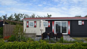 A two-story house with a red-tiled roof, a covered patio with a table and chairs, and a fenced garden area. - Chalet Zonnebloem for 6 people, lots of privacy in a quiet park (Serooskerke (W))