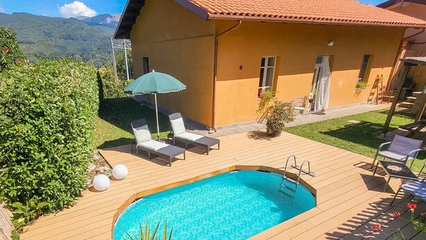 Un área junto a la piscina con sillones de descanso, una piscina pequeña y un edificio con tejado de azulejos.