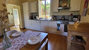 Una cocina con armarios blancos, microondas, estufa y lavabo. Se ve un ventanal con vistas a zonas verdes.