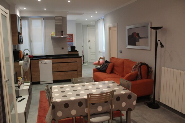 A compact living space with a kitchenette, a dining area with a polka dot tablecloth, and a cozy orange sofa.
