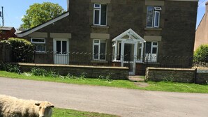 A stone house with a well-maintained lawn and a sheep in the foreground. - 🌿 Peaceful & Cosy Cottage Stay in the Forest of Dean 🌳🐑 (Lydney)