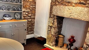 A stone-walled room with a fireplace, a dining table, and a red rug. - 🌿 Peaceful & Cosy Cottage Stay in the Forest of Dean 🌳🐑 (Lydney)