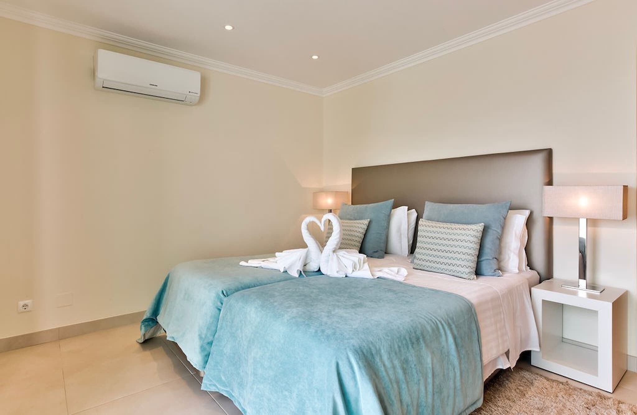 A hotel room with a bed, a nightstand, a lamp, and an air conditioning unit.
