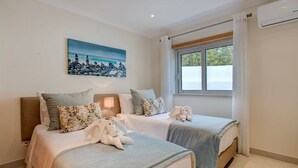 A hotel room with two beds, a painting on the wall, a window with curtains, and an air conditioning unit. - Bay H Modern townhouse very central, fabulous sea views! (Carvoeiro)