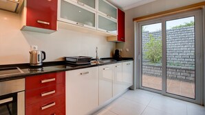 A modern kitchen with red and white cabinetry, a black countertop, and a large sliding glass door leading to a patio with a brick wall and greenery. - Bay H Modern townhouse very central, fabulous sea views! (Carvoeiro)