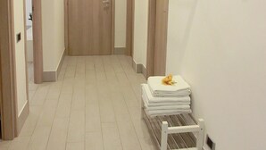 En gang med en trædør i enden, et hvidt håndklædetørrestativ med foldede håndklæder og en lille hvid bænk.