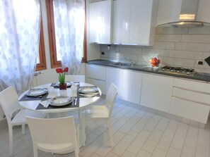 A modern kitchen with white cabinets, a stainless steel sink, and a gas stove. There is a dining table with white chairs and a vase with red flowers. - adjacent to the Biennale, a short distance from St. Marco, characteristic area (Venezia)