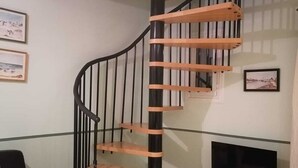 A modern living room with a spiral staircase, a black leather sofa, a television on a wooden stand, and framed pictures on the wall. - Cottage with private garden in wooded property with swimming pool (Pertuis)