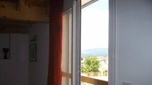 A room with a sliding glass door leading to a balcony with a view of a cityscape and mountains. - Cottage with private garden in wooded property with swimming pool (Pertuis)