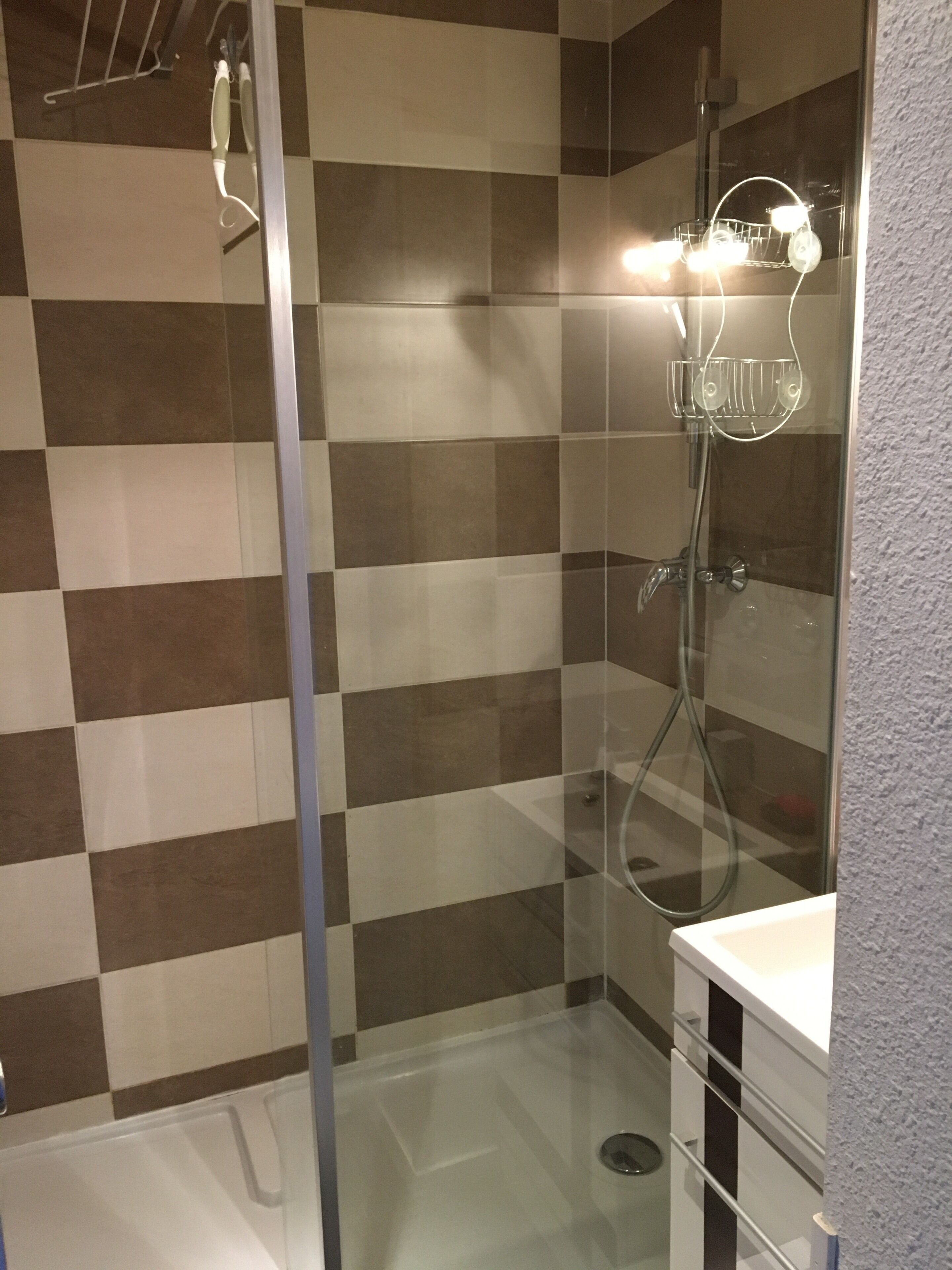 Un espace douche doté d’une porte en verre, de murs carrelés à motifs et d’un plan de travail blanc.