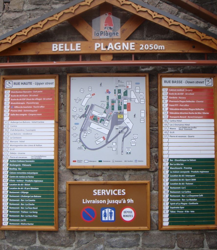 Un panneau indicateur avec un plan et une liste des services et des commodités disponibles à Belle Plagne (2050 m d'altitude), comprenant les indications pour les rues du haut et du bas, ainsi qu'une section consacrée aux services, avec leurs heures d'ouverture.