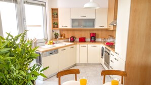 A modern kitchen with white cabinets, a red coffee maker, and a dining table with two chairs.