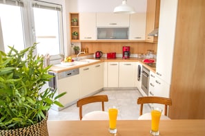 A modern kitchen with white cabinets, a red coffee maker, and a dining table with two chairs. - Athens Luxurious Apartment - Sea View!  (Paleo Faliro)