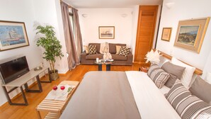 A modern hotel room with a large bed, a sofa, a TV, and a dining area.