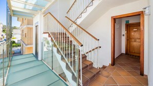 Un intérieur moderne avec un escalier en verre, une porte en bois et une vue sur l’extérieur.