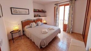 Une chambre bien rangée, avec un grand lit, des tables de chevet, une bibliothèque et un balcon agrémenté de rideaux.
