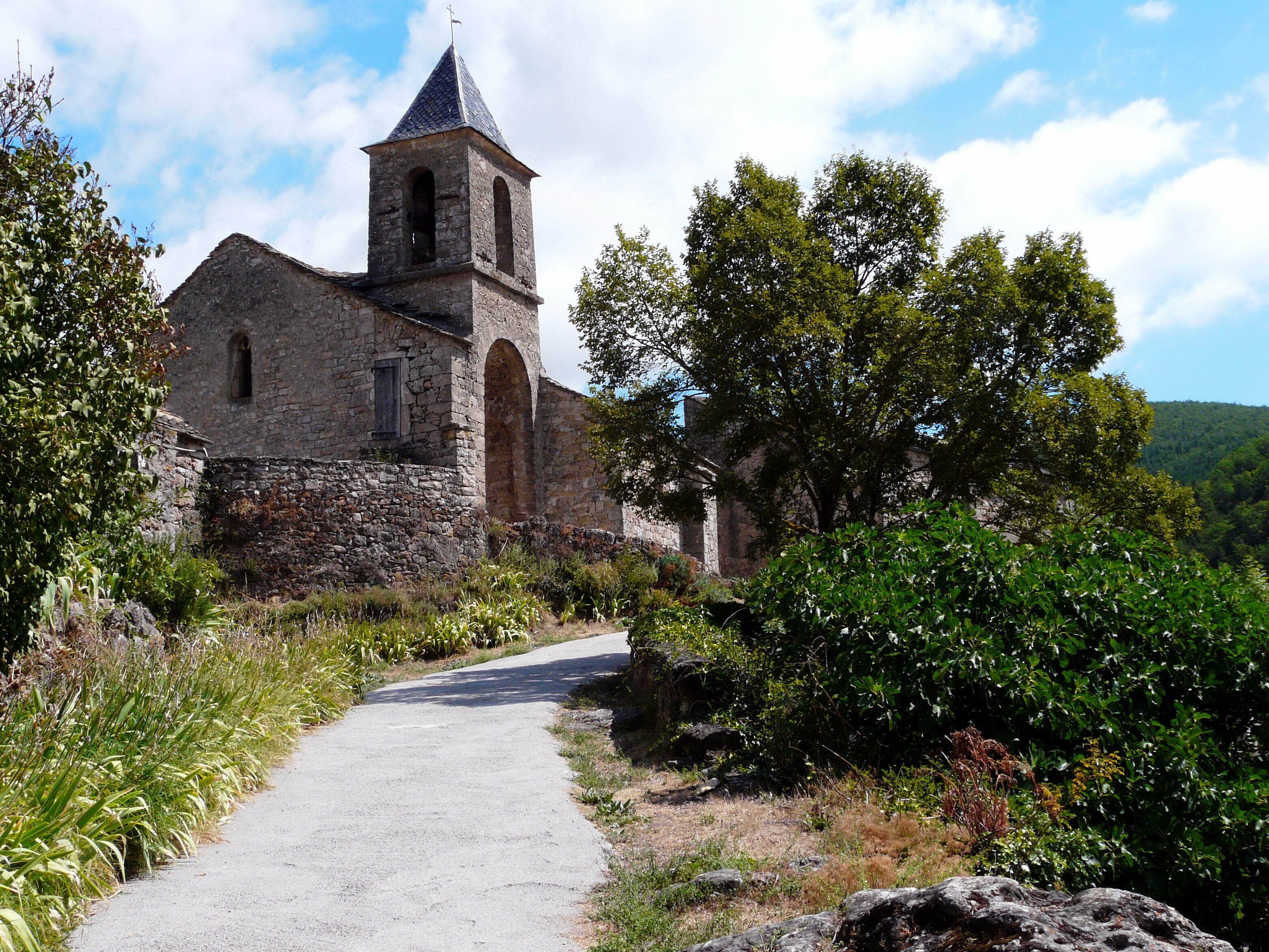 Une église en pierre dotée d’un clocher et d’un chemin pavé menant à l’entrée, le tout entouré de verdure.