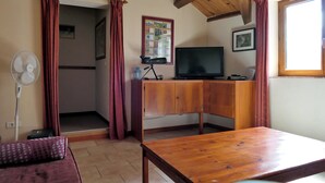 A room with a wooden table, a TV on a wooden cabinet, a fan, and a window with curtains. - Stunning Valley Views from our 3* Gîte bordering the Cévennes and Grands Causses (Nant)