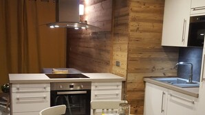Eine kleine Küche mit weißen Schränken, einem eingebauten Backofen und einem Spülbecken. Ein Esstisch mit Stühlen und einer gelben Tischdecke ist ebenfalls vorhanden.