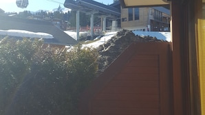 Blick von einer überdachten Veranda mit einem roten Stuhl, einem Gebäude mit geneigtem Dach und einer Seilbahn im Hintergrund.