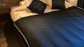 Ein Schlafzimmer mit einem großen Bett, zwei schwarze Kissen mit Schneeflockenmuster und einem weißen, flauschigen Kopfkissen, sowie einem Holzkopfbrett.