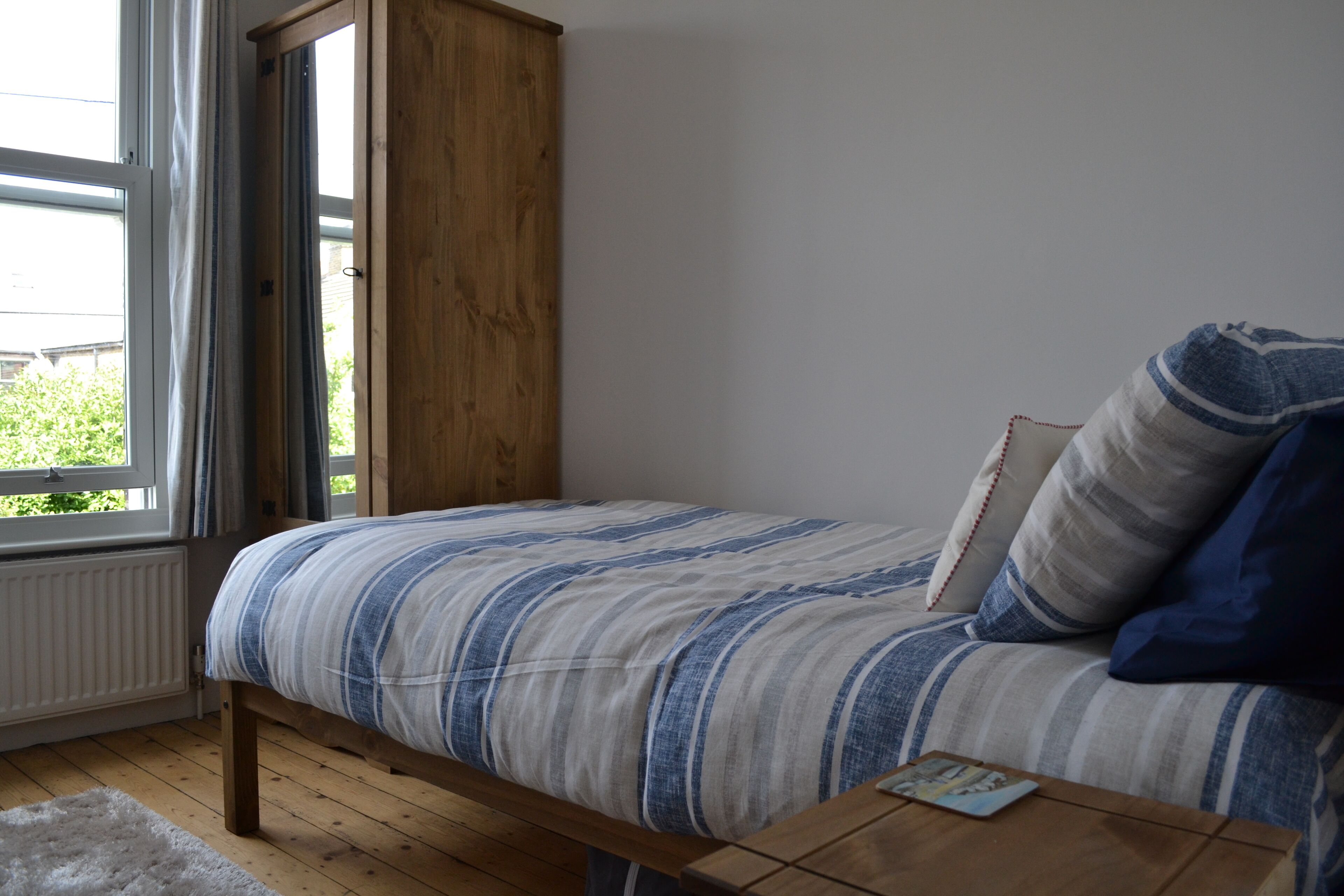 A bedroom with a bed, wooden floor, window, and a small table.