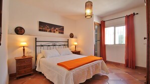 Ein Schlafzimmer mit einem Bett, zwei Nachttischen, einer Stehlampe, einem Fenster mit Vorhängen und einem Stadtbild an der Wand.
