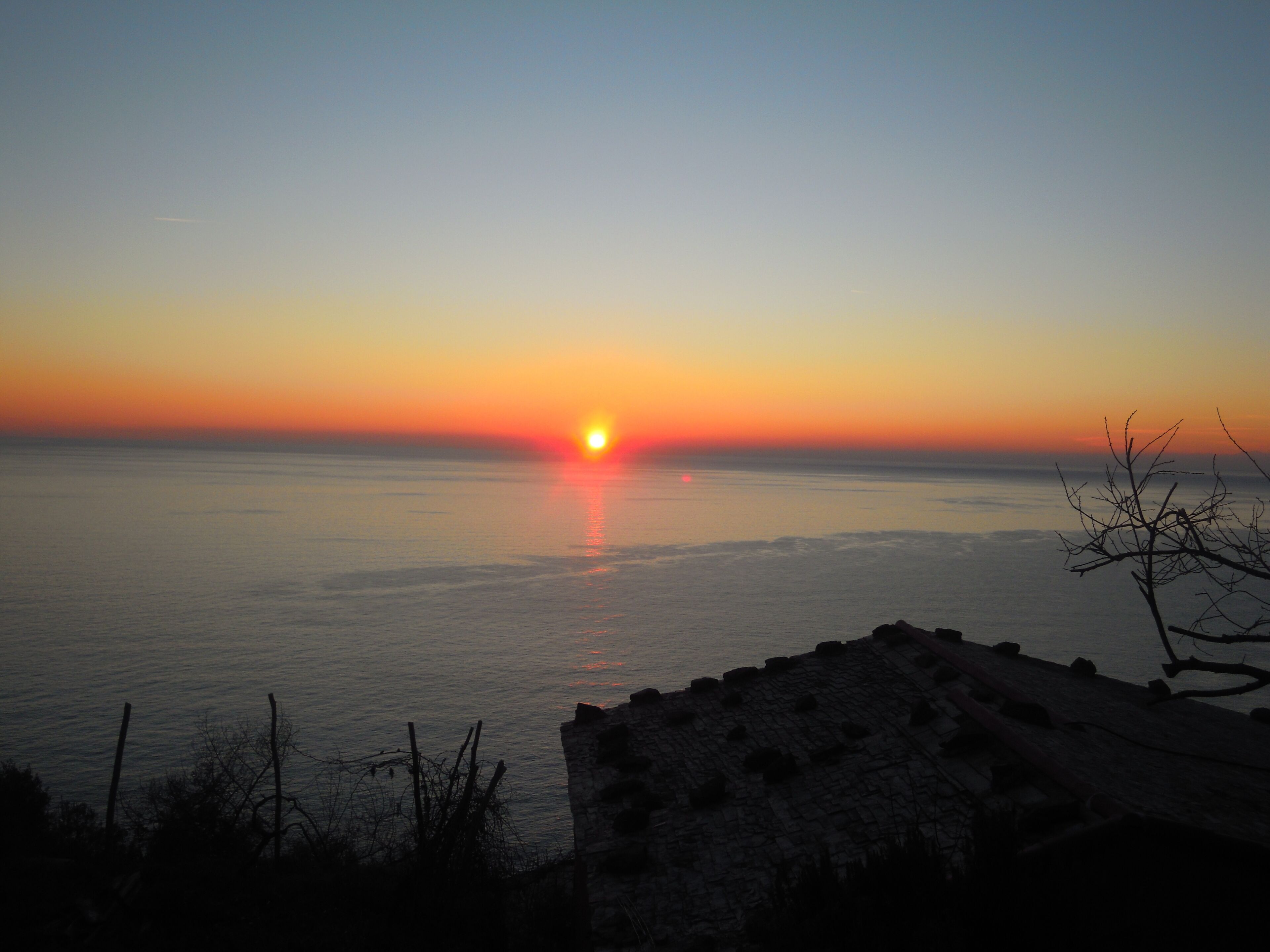 Ein Sonnenuntergang über einem ruhigen Meer mit einer felsigen Küste im Vordergrund.